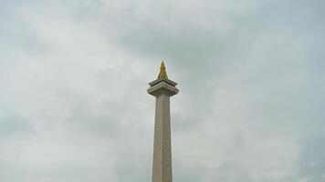 The iconic Monas in Jakarta stands tall against a backdrop of beautiful clouds and lush green grass photo