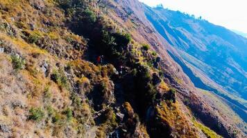On the trek to Mount Rinjani's summit, a path of lush green and brown grass unfolds beneath a brilliant blue sky. Rest stops dot the route. photo