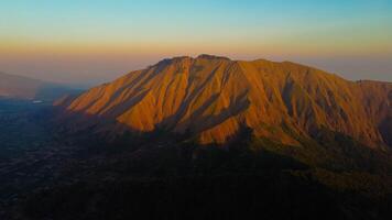 Experience breathtaking aerial views of the rolling hills in Sembalun, at the foot of Mount Rinjani, with expansive savanna turning golden at sunrise. photo