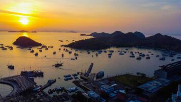 Aerial view of Labuan Bajo harbor at sunset, showcasing numerous pinisi boats docked, with charming local residences surrounding the vibrant scene. photo