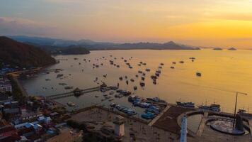 Aerial view of Labuan Bajo harbor at sunset, showcasing numerous pinisi boats docked, with charming local residences surrounding the vibrant scene. photo