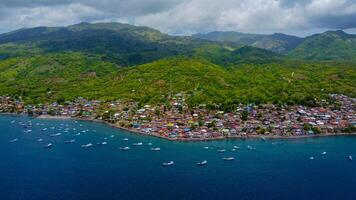 Aerial view of Labuan Bajo harbor at sunset, showcasing numerous pinisi boats docked, with charming local residences surrounding the vibrant scene. photo