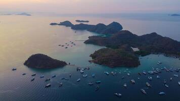 Aerial view of Labuan Bajo harbor at sunset, showcasing numerous pinisi boats docked, with charming local residences surrounding the vibrant scene. photo
