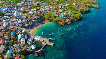 Aerial view of Labuan Bajo harbor at sunset, showcasing numerous pinisi boats docked, with charming local residences surrounding the vibrant scene. photo