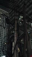A chaotic bundle of tangled power cables and electrical connections on a utility pole in a densely populated urban area. photo