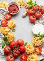 Italian food background featuring tomatoes, pasta, garlic, cheese, basil and tomato sauce creating a frame photo