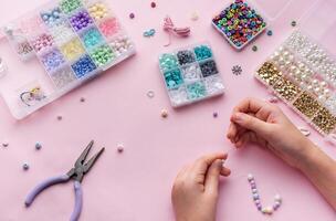 Creating colorful beaded jewelry with assorted beads and crafting tools on a light pink surface photo