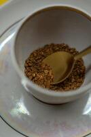A spoonful of coffee in a mug on a saucer on a yellow background. Close up photo