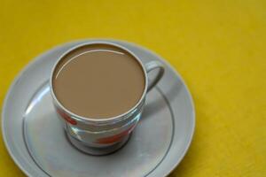 A mug of coffee with milk. Mug in a saucer on a yellow background. Top-down view photo