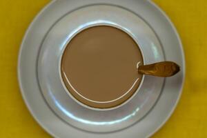 A spoon in a mug with coffee and milk. A mug in a saucer on a yellow background photo