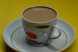 A mug of coffee with milk. Mug in a saucer on a yellow background. Top-down view photo