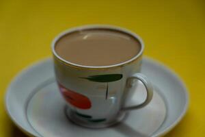 A mug of coffee with milk. Mug in a saucer on a yellow background. Top-down view photo