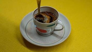 Stirring coffee with a spoon in a mug. A mug in a saucer on a yellow background photo