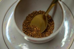 A spoonful of coffee in a mug on a saucer on a yellow background. Close up photo