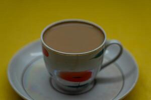 A mug of coffee with milk. Mug in a saucer on a yellow background. Top-down view photo