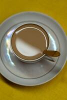 A spoon in a mug with coffee and milk. A mug in a saucer on a yellow background photo
