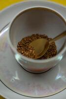 A spoonful of coffee in a mug on a saucer on a yellow background. Close up photo