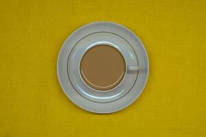 A mug of coffee with milk. Mug in a saucer on a yellow background. Top-down view photo
