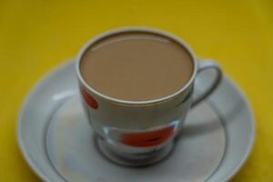 A mug of coffee with milk. Mug in a saucer on a yellow background. Top-down view photo