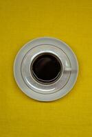 Instant coffee in a mug. A mug in a saucer on a yellow background. Top-down view photo
