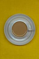 A mug of coffee with milk. Mug in a saucer on a yellow background. Top-down view photo