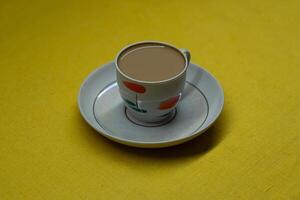 A mug of coffee with milk. Mug in a saucer on a yellow background. Top-down view photo