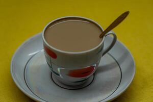 A spoon in a mug with coffee and milk. A mug in a saucer on a yellow background photo