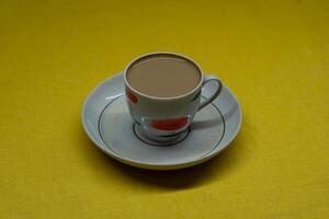 A mug of coffee with milk. Mug in a saucer on a yellow background. Top-down view photo
