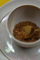A spoonful of coffee in a mug on a saucer on a yellow background. Close up photo