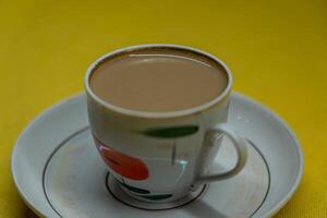A mug of coffee with milk. Mug in a saucer on a yellow background. Top-down view photo