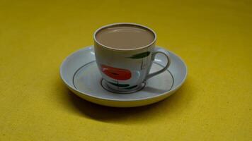A mug of coffee with milk. Mug in a saucer on a yellow background. Top-down view photo
