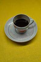 Instant coffee in a mug. A mug in a saucer on a yellow background. Top-down view photo