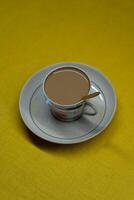 A spoon in a mug with coffee and milk. A mug in a saucer on a yellow background photo