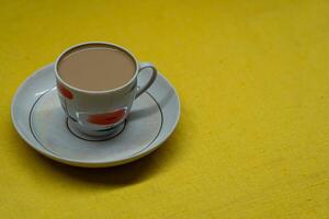 A mug of coffee with milk. Mug in a saucer on a yellow background. Top-down view photo