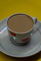 A mug of coffee with milk. Mug in a saucer on a yellow background. Top-down view photo