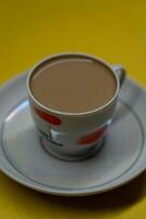 A mug of coffee with milk. Mug in a saucer on a yellow background. Top-down view photo