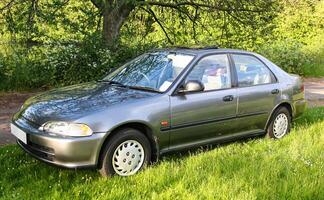 Classic dark silver sedan is parked on a grassy patch with trees and foliage in the background, the scene conveys a peaceful, natural setting with vibrant green surroundings photo