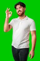 A smiling man in a white polo shirt makes an okay gesture against a bright green background photo