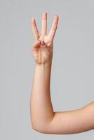A hand showing the number three with fingers raised against a light gray background photo