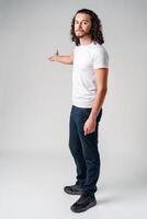 Young man in a white t-shirt and jeans pointing confidently while smiling in a studio setting photo