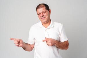 Man dressed in a white polo shirt and jeans happily pointing to the side against a plain background photo