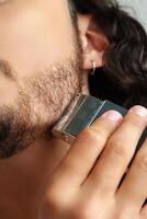 Man trimming his beard indoors using an electric trimmer while showcasing his personal grooming routine photo