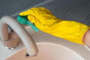 Hands in yellow gloves cleaning a sink with a sponge photo