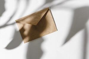 Paper envelope on white background with leaf shadow, top view photo