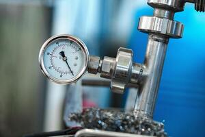 A pressure gauge is attached to a metal pipe in a factory setting photo