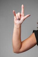 A person making the I love you gesture with their hand in front of a neutral gray background photo
