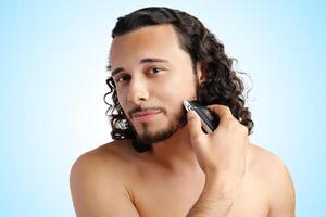 A young man with curly hair grooming his beard using an electric trimmer photo