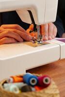 Hands sewing fabric using a sewing machine on a wooden table in a well-lit workspace photo