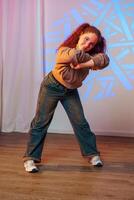 A young woman with red hair dances in a studio, her body contorted in a dynamic pose photo
