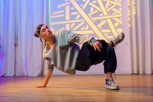 A dancer performs a breakdancing move in a studio with white curtains and a geometric light projection on the wall photo